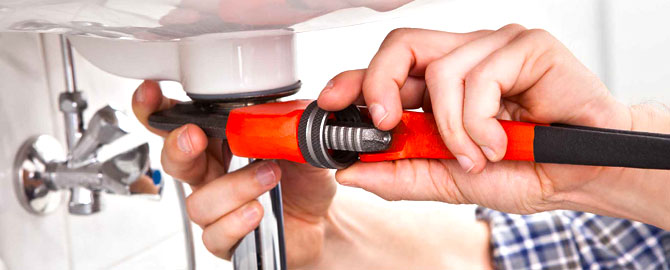 hands of a scarborough plumbing contractor holding a wrench while working on the drain of a bathroom sink
